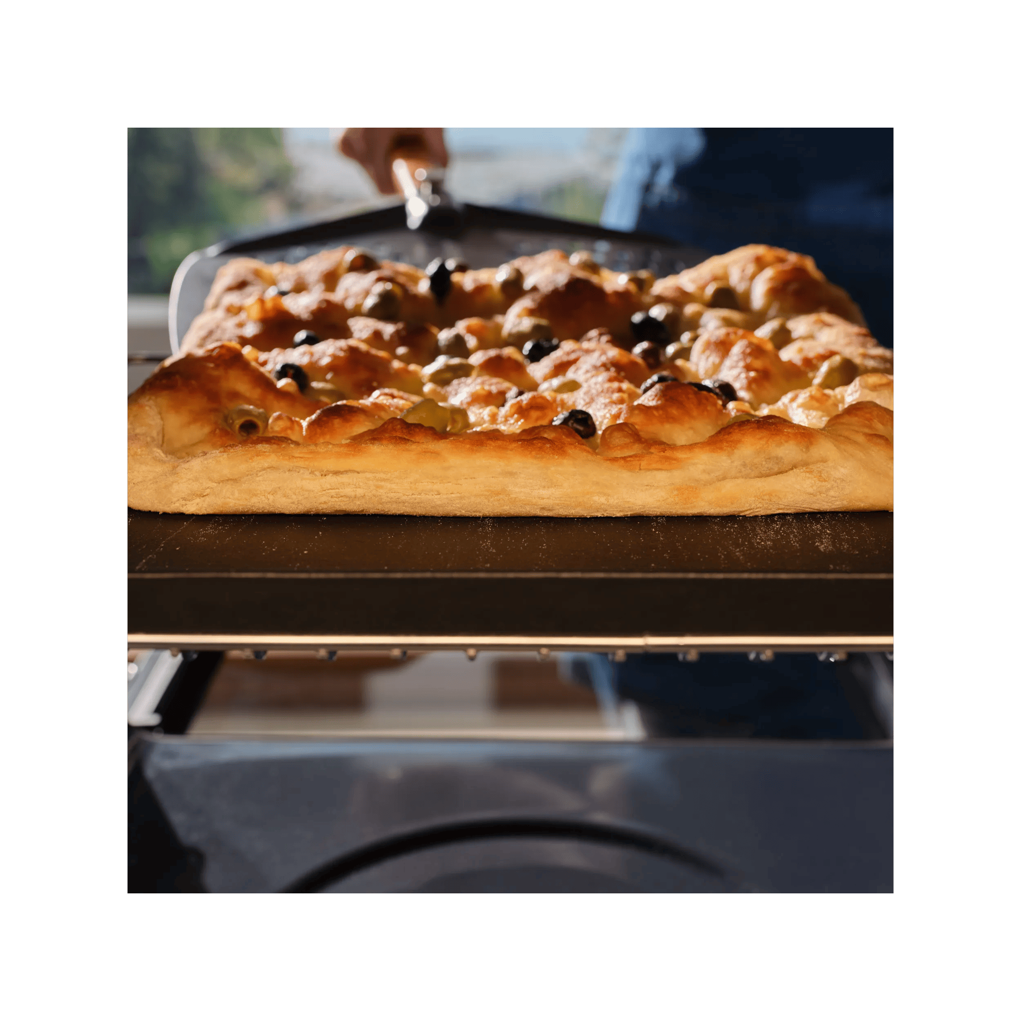 A focaccia baking inside the pizza expert oven with a pizza peel underneath 