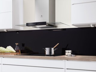 En skorstensfläkt i glas och rostfritt stål ovanför en kastrull på en induktionshäll