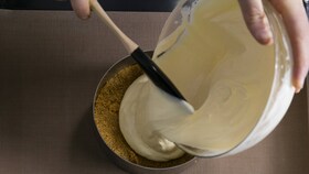 En bagare häller i den fina cheesecake-blandningen i en rund form, redo för ugnen