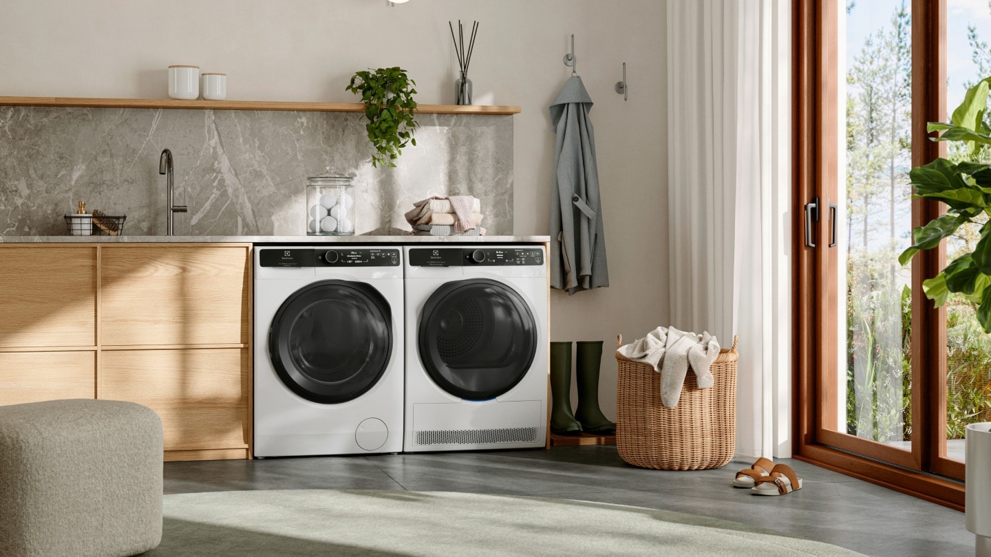 Tvättstuga med en tvättmaskin och torktumlare från Electrolux bredvid varandra under en bänk.
