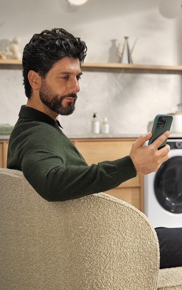 En man sitter på en stol med en telefon i handen och en tvättmaskin i bakgrunden.