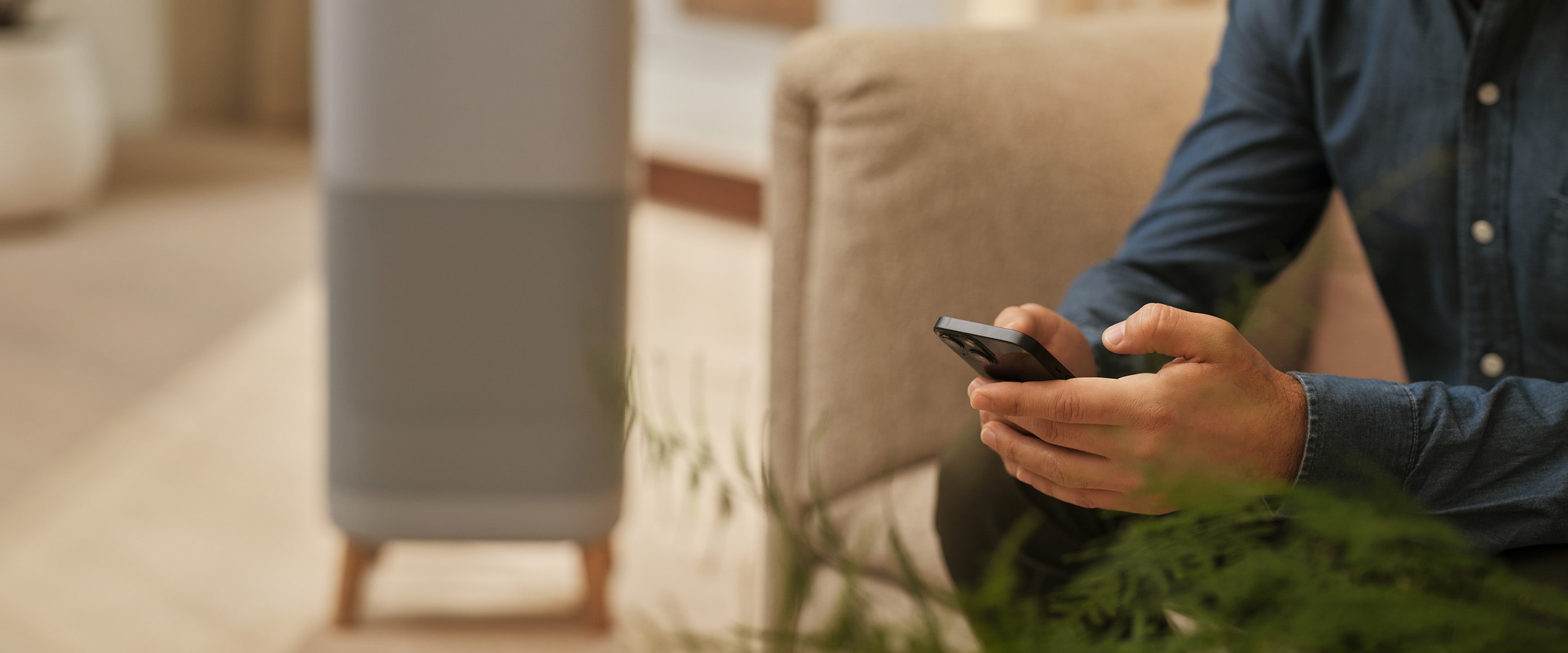 Man som håller i en mobiltelefon med en luftrenare i bakgrunden
