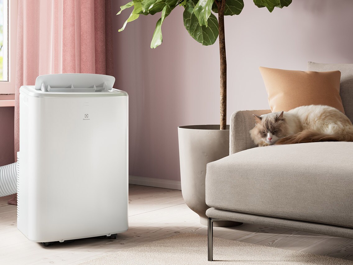 En vit portabel Electrolux-luftkonditionering i ett ljust vardagsrum med en sovande katt i soffan.