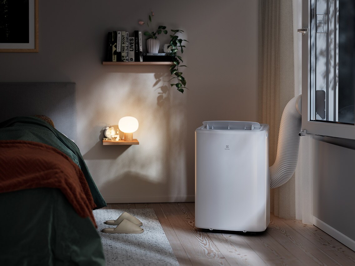 Vit portabel Electrolux-luftkonditionering med fönsteranslutning i ett sovrum.