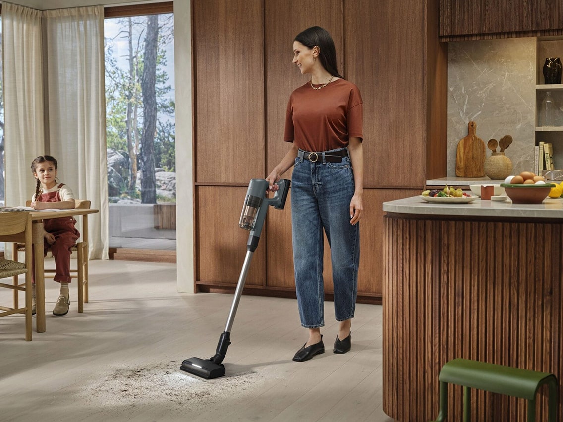 En kvinna använder en sladdlös Electrolux 700-dammsugare för att städa ett ljust trägolv i ett modernt kök.