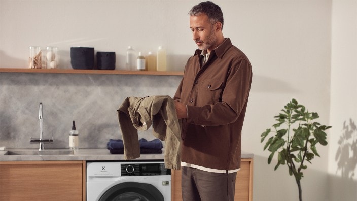 Man viker tvätt framför tvättmaskin