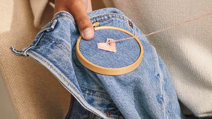 Litet hjärta i tyg som sys fast på ett par jeans