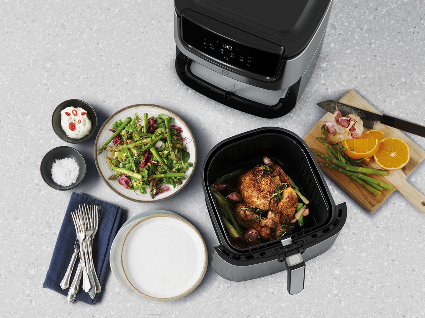 En hel kyckling och grönsaker ligger tillagade bredvid en Airfryer.
