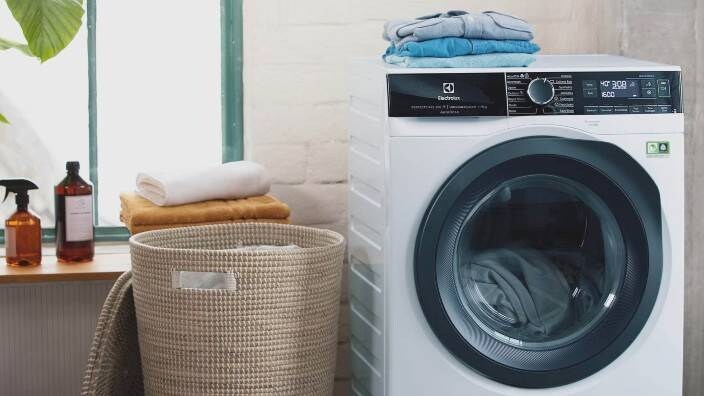 En tvättmaskin från Electrolux tvättar kläder. Ovanpå ligger snyggt hopvikta plagg.