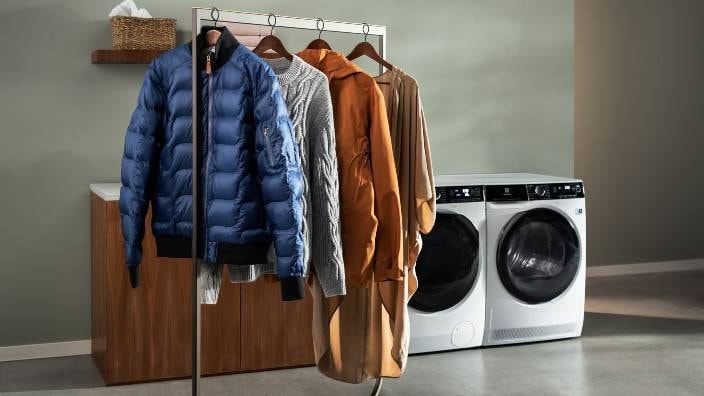 Fyra klädesplagg hänger på tork framför en torktumlare och tvättmaskin från Electrolux.