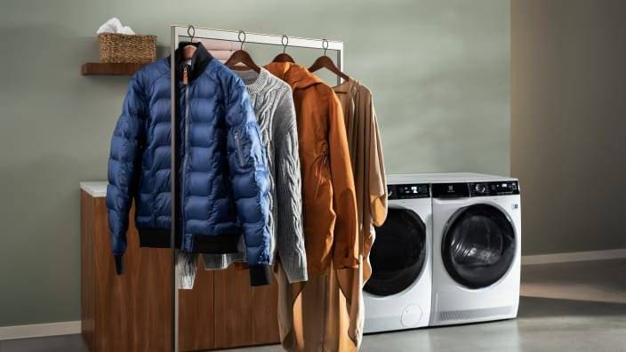 Prydligt upphängda plagg på tork framför en tvättmaskin och torktumlare från Electrolux.